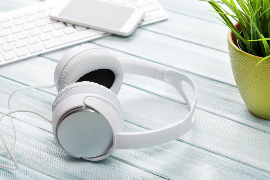 Fones de ouvido brancos, teclado e planta. Problemas comuns em fones TWS.